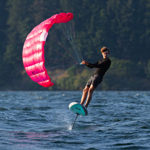 Person kitesurfing on water with a pink kite and hydrofoil board.